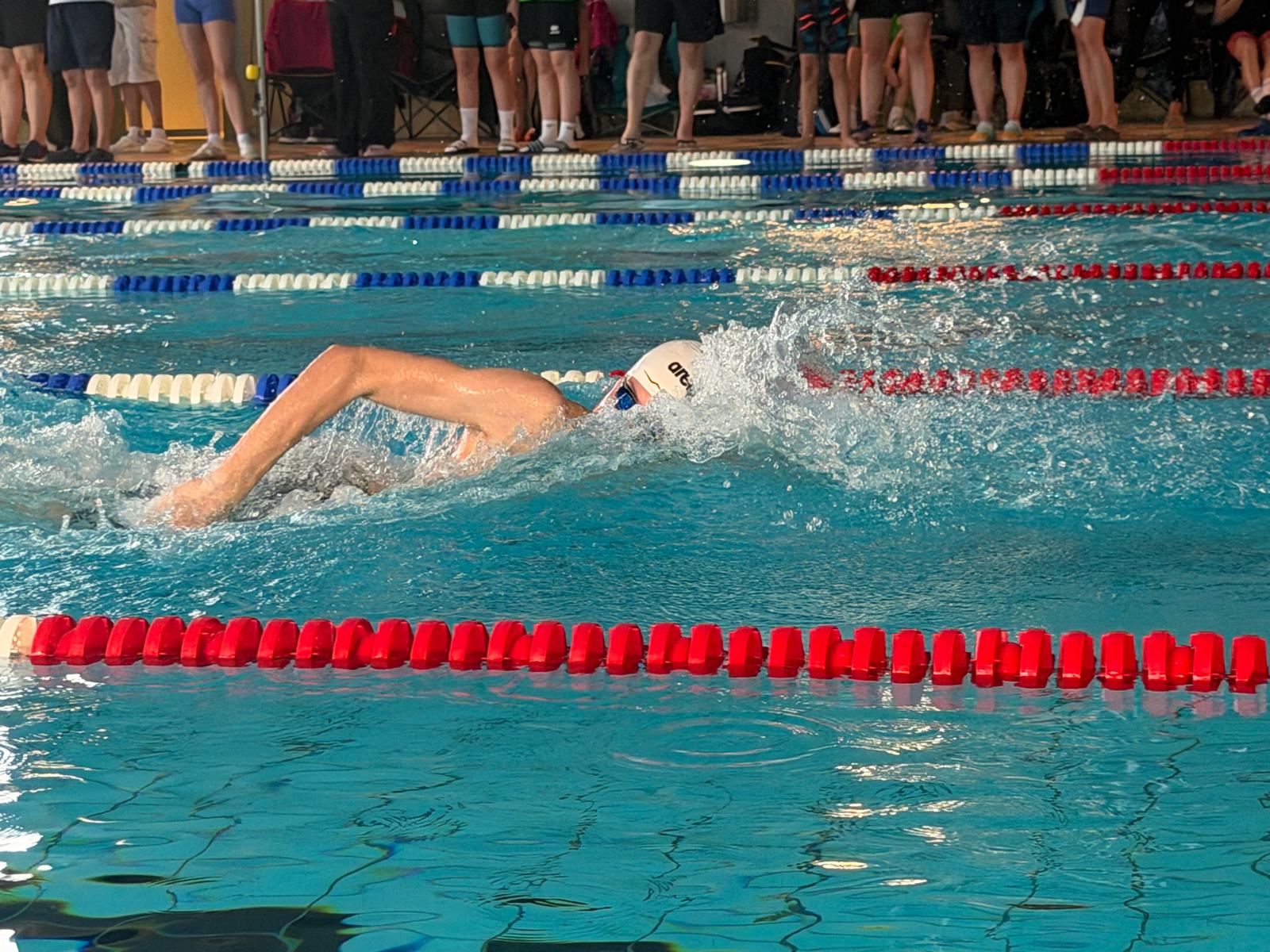 Ein Schwimmer mit weißer Badekappe und blauer Schwimmbrille beim Kraulschwimmen.